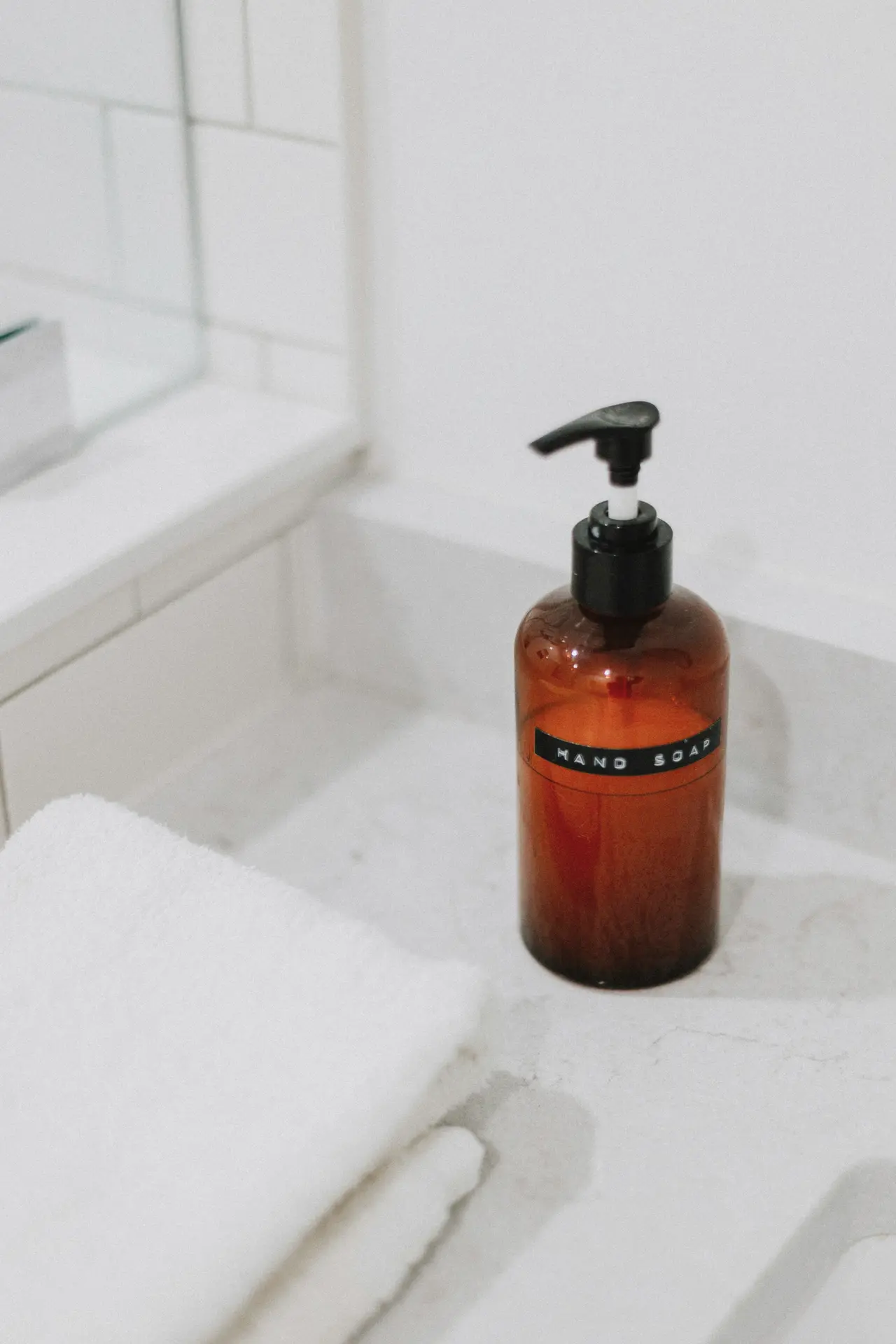 An amber soap bottle and a folded white towel beside a bath