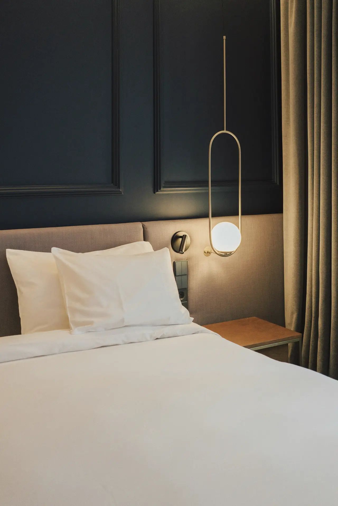 A calm bedroom with white linen and a brass pendant light