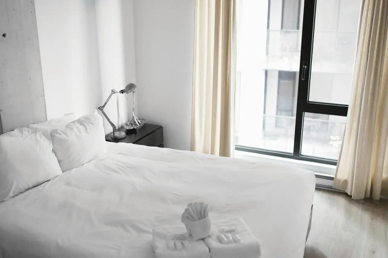 A made bed beside tall windows in a bright apartment bedroom