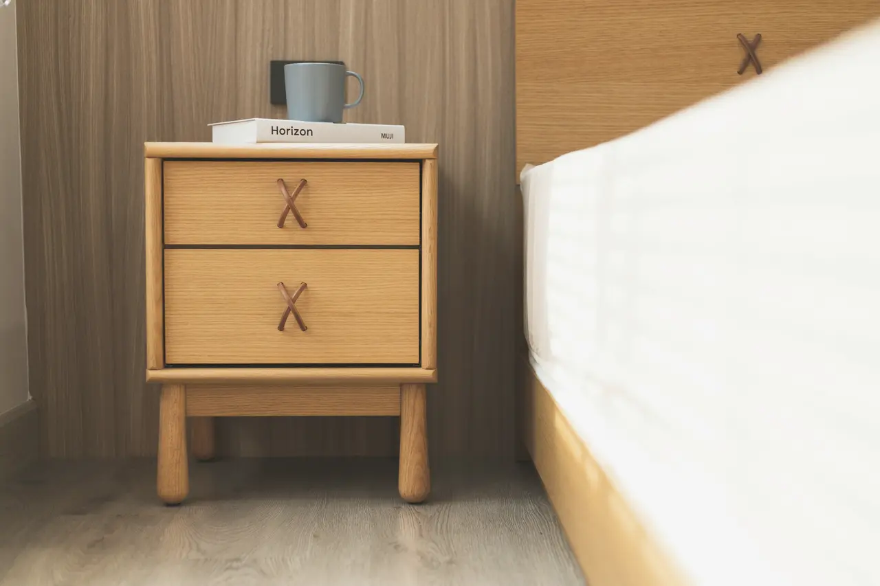 A timber bedside table beside a neatly made bed