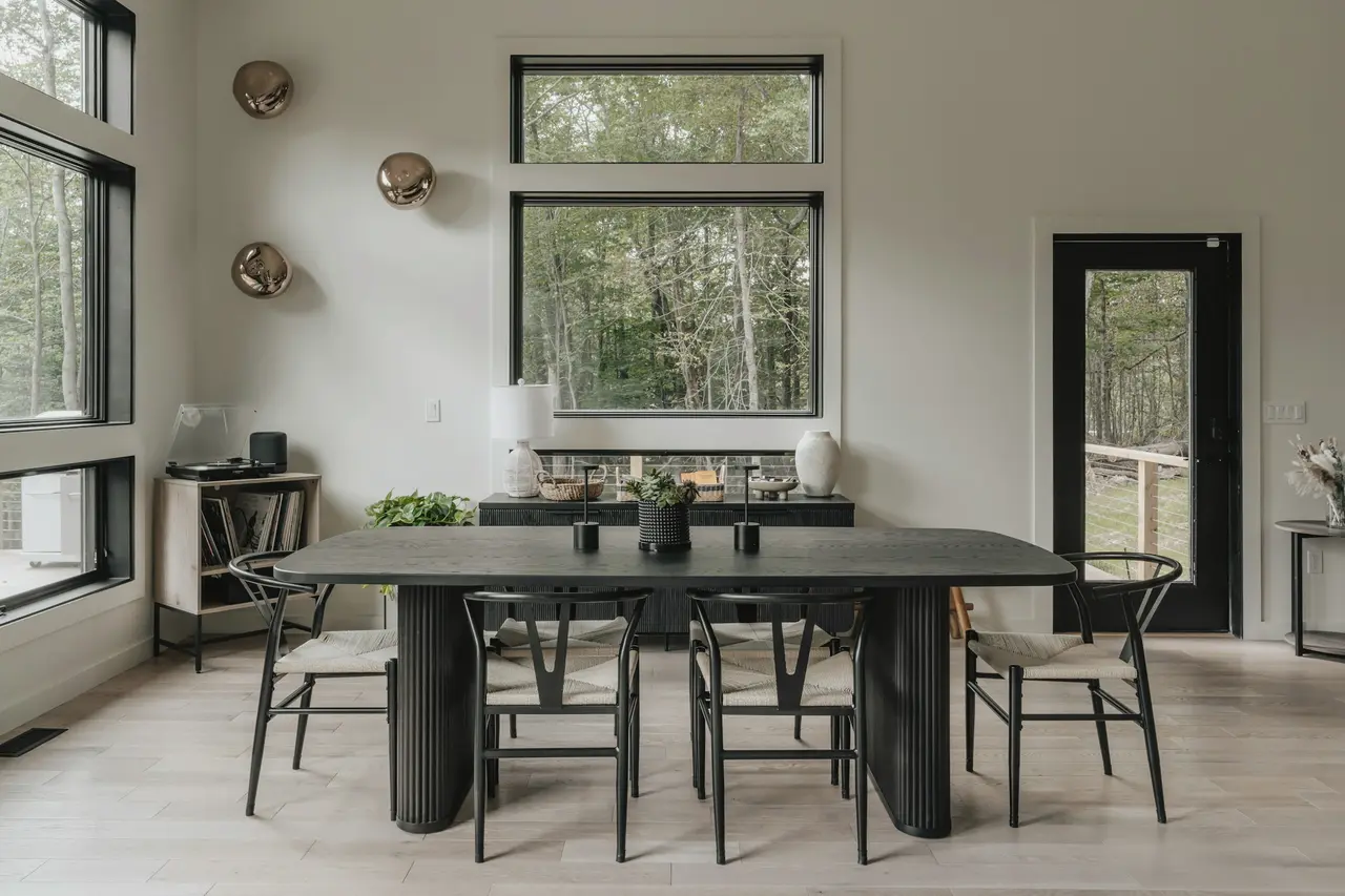 A dining room with a dark table, chairs and garden views