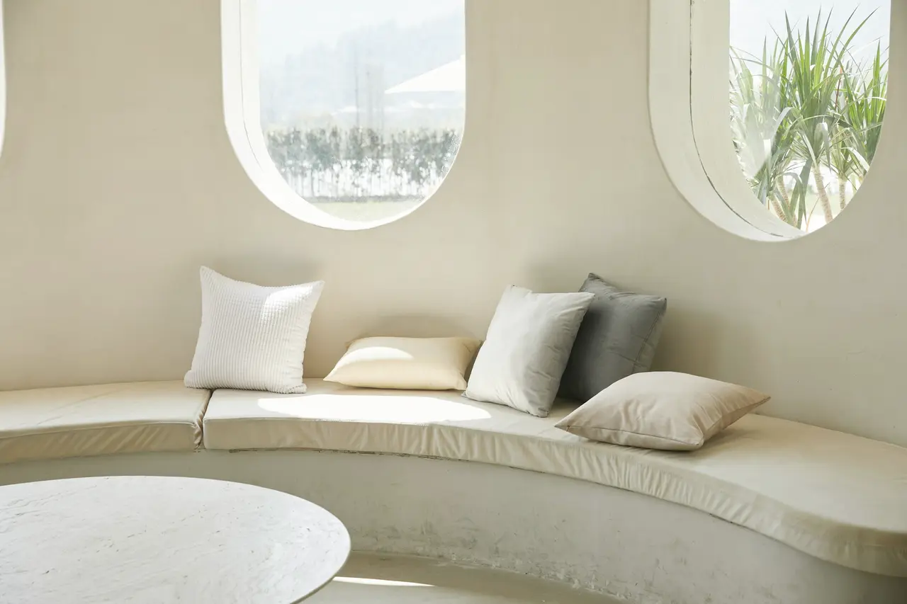 A curved window seat with cushions in a pale, quiet room
