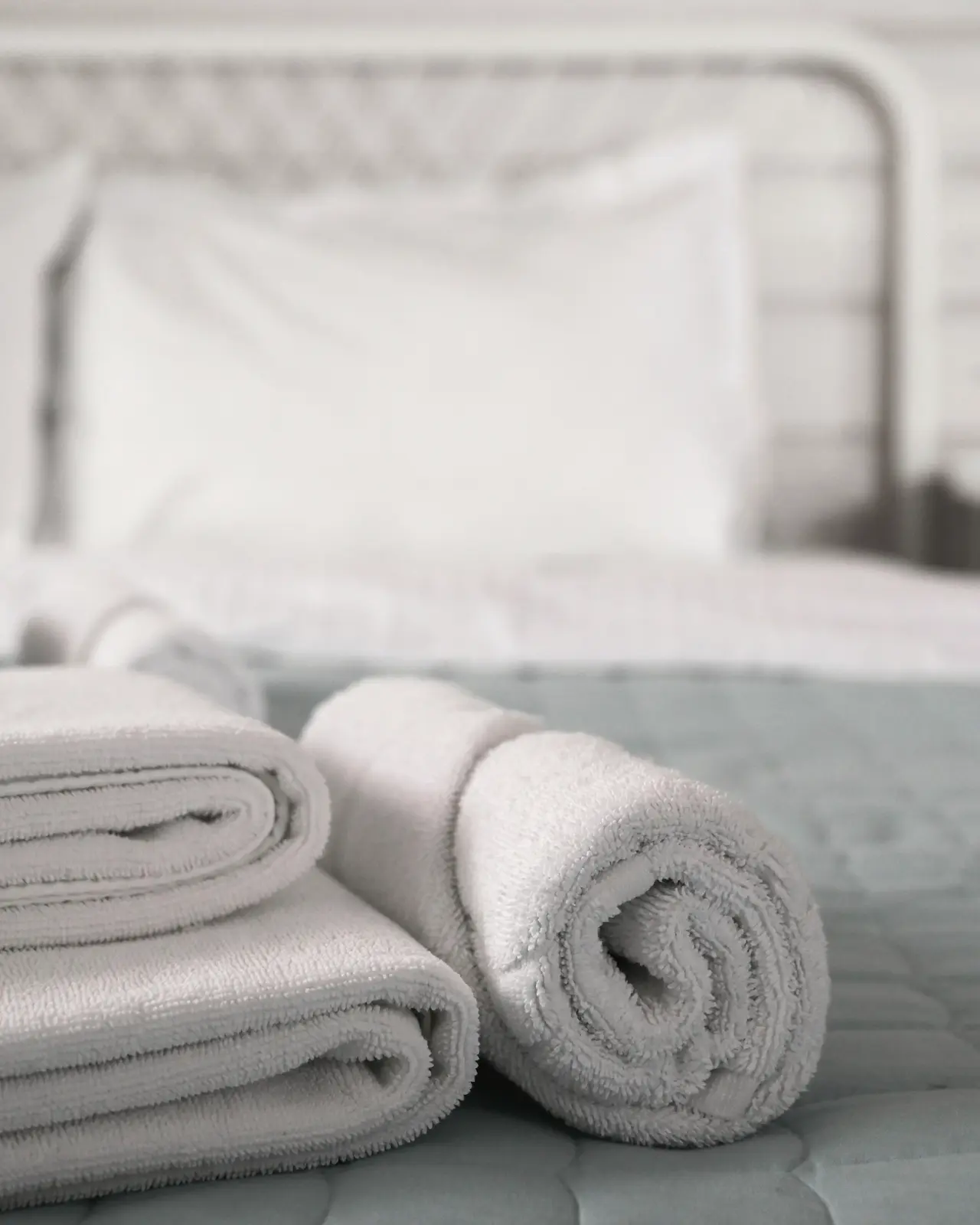 Rolled white towels at the end of a made bed